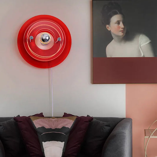 Red circular wall light fixture on a white wall above a gray sofa with pillows.