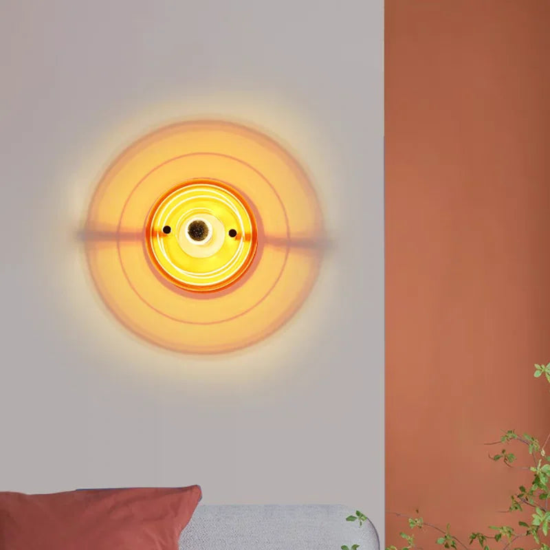 Round wall light fixture with a warm glow on a wall next to a plant.